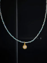 Halskette mit blauen Glasperlen, in der Mitte ist ein kleiner goldener Sonnenanhänger mit kleinen Zirkonia Steinen